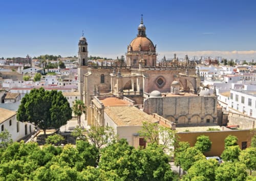Catedral y edificios blancos en Medina Sidonia, España con árboles verdes y cielo azul despejado