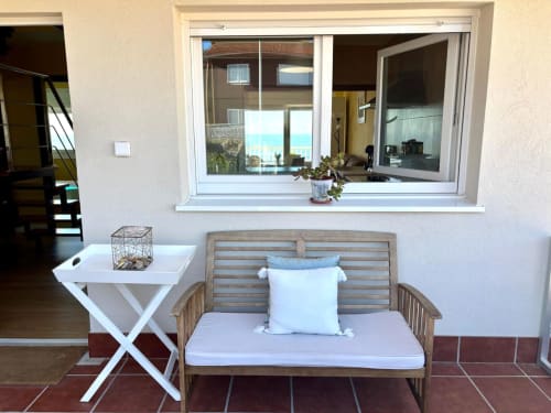 Banco de madera con cojín y almohada azul en la terraza de Holibai Baiona, vistas al mar por la ventana