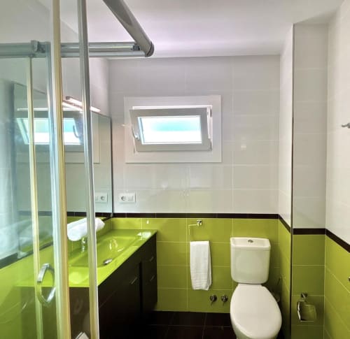Baño moderno en Holibai Albatros Dúplex, Baiona con azulejos verde lima, detalles negros, lavabo, inodoro y ducha con cristal