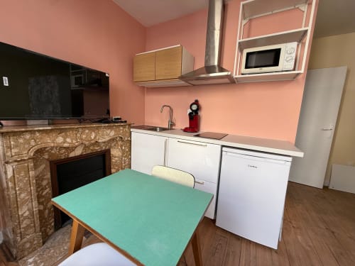Gemütliche renovierte Studio-Küche in Lourdes mit türkisem Esstisch, rosa Wänden, weißen Geräten und Kamin