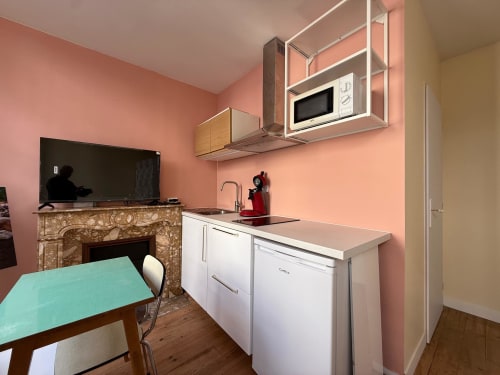 Gemütliches renoviertes Küchenstudio in Lourdes mit rosa Wänden, weißen Geräten, Mikrowelle, Esstisch und Kamin.