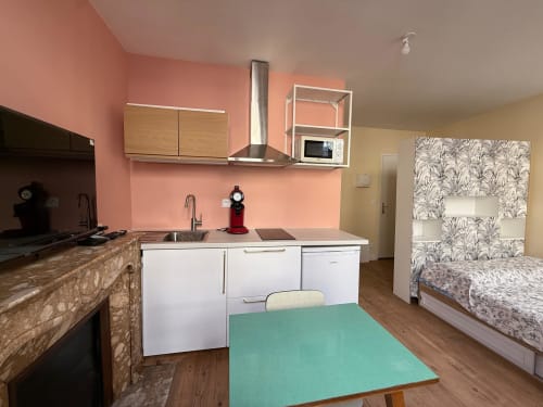Modernes Studio-Küchenkonzept mit rosa Wänden, weißen Schränken und grünem Esstisch in einem Hotelapartment in Lourdes