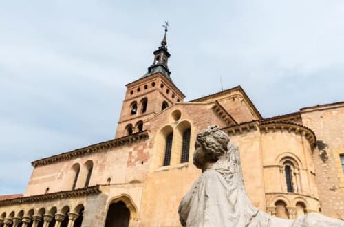 Iglesia de piedra con campanario en Nieva, España. Estatua en primer plano. Alojamiento Tradición Rural cercano.