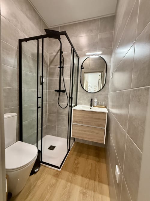 Modern bathroom in Casa Tawny with black-framed shower enclosure, wooden vanity, and beige tile walls in Pinhão, Portugal
