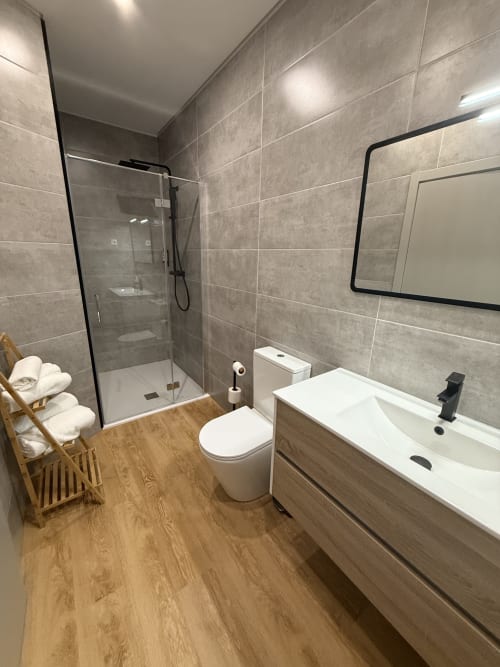 Modern bathroom at Casa Tawny with vanity sink, toilet, walk-in shower, wooden floor, and towel rack in Pinhão, Portugal