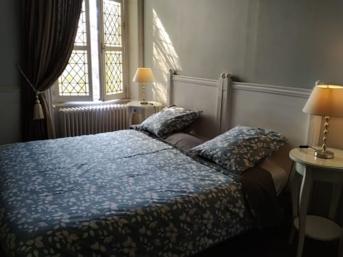 Chambre élégante au Château de Bellevue avec literie bleue à motifs, tête de lit blanche, lampes en laiton et vue sur le jardin