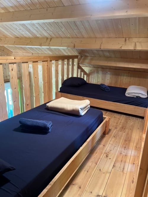 Due letti in legno con biancheria blu navy e asciugamani arrotolati in una luminosa lodge in legno presso Cabanes et lodges du Belvédère