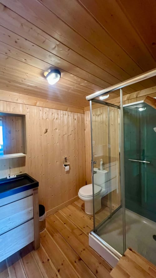 Bagno moderno nel Lodge LE TAILLET con pareti in legno, doccia in vetro, wc e illuminazione LED presso Cabanes et lodges