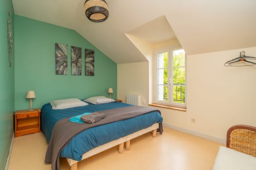 Chambre lumineuse à Vacances en Touraine avec murs vert menthe, literie bleue, mobilier en bois et vue sur le jardin