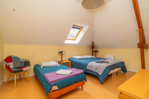 Chambre lumineuse sous les toits à Vacances en Touraine avec deux lits bleus, murs jaunes et fenêtres de toit à Souvigny-de-Touraine.