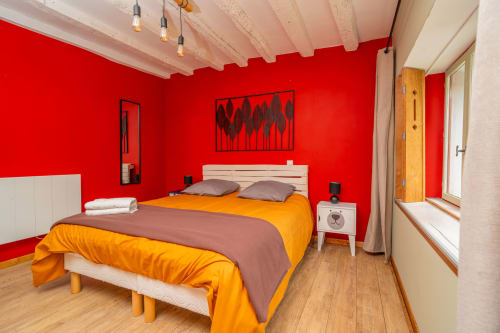 Chambre d'un rouge éclatant aux Vacances en Touraine avec literie orange, poutres en bois et équipements modernes à Souvigny-de-Touraine