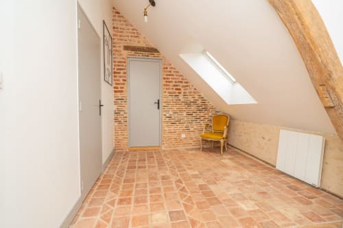 Chambre mansardée lumineuse avec carrelage en terre cuite, briques apparentes, poutre en bois et chaise jaune aux Vacances en Touraine