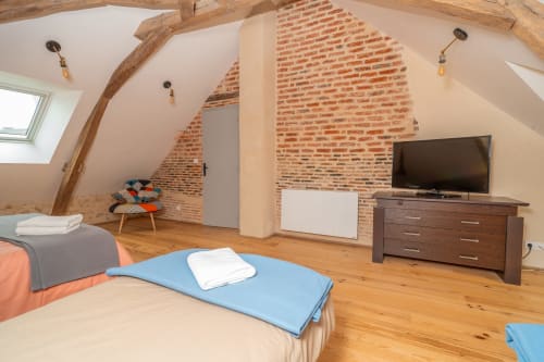 Spacieuse chambre mansardée à Vacances en Touraine avec poutres apparentes, murs en briques, parquet, TV et mobilier moderne.