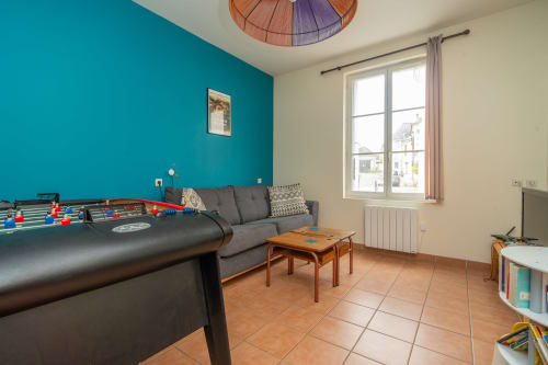Salle de jeux avec baby-foot, canapé gris et mur d'accent turquoise aux Vacances en Touraine