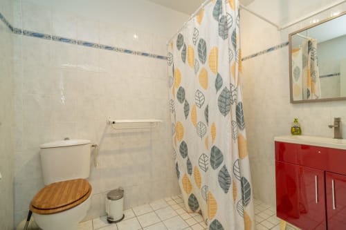 Salle de bain moderne avec rideau de douche motif feuillage, vanité rouge et abattant toilettes en bois à l'hôtel Vacances en Touraine