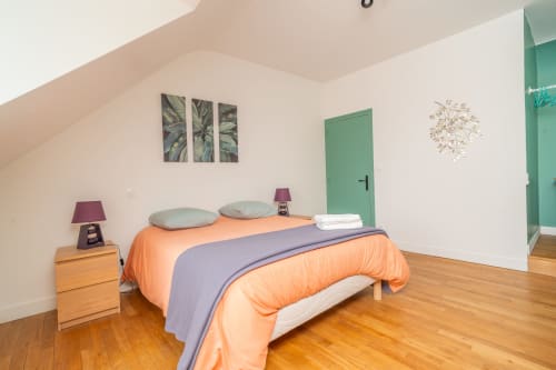 Chambre lumineuse à Vacances en Touraine avec literie orange, porte verte, table de nuit en bois et décor botanique mural.