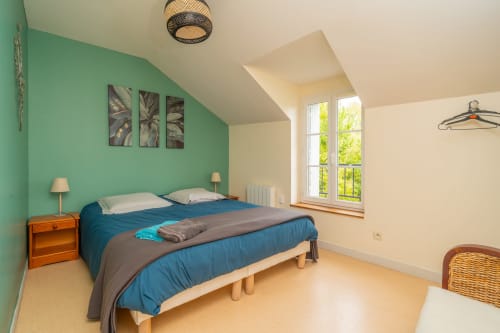 Chambre lumineuse du gîte Vacances en Touraine avec mur turquoise, lit double, grande fenêtre, table de nuit en bois et poutres