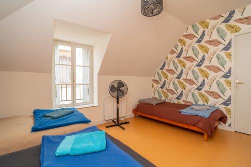 Chambre lumineuse sous les combles du gîte Vacances en Touraine avec deux lits bleus, sol orangé, papier peint à motifs de feuilles et plafond mansardé