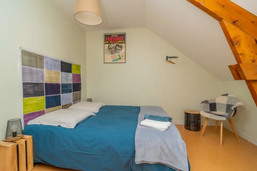 Chambre lumineuse sous les combles aux Vacances en Touraine, avec tête de lit colorée, literie bleue, poutres en bois et mobilier moderne
