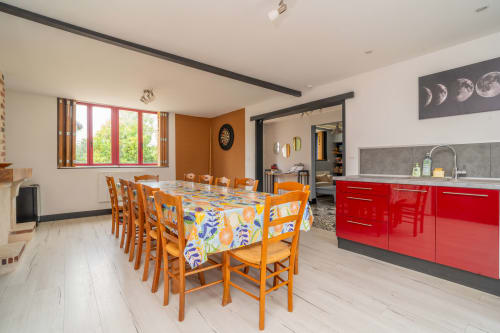 Salle à manger lumineuse avec chaises oranges, nappe colorée et armoires de cuisine rouges au gîte Le Charme
