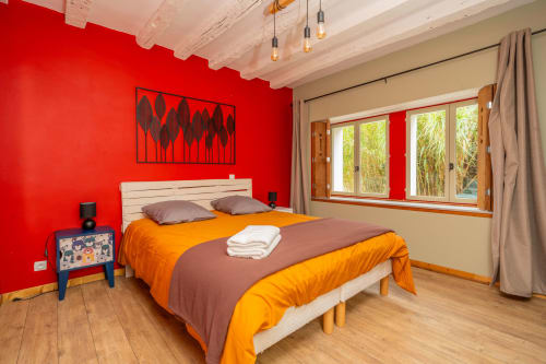 Chambre lumineuse du gîte Le Charme à Souvigny-de-Touraine avec mur d'accent rouge, literie orange et grandes fenêtres