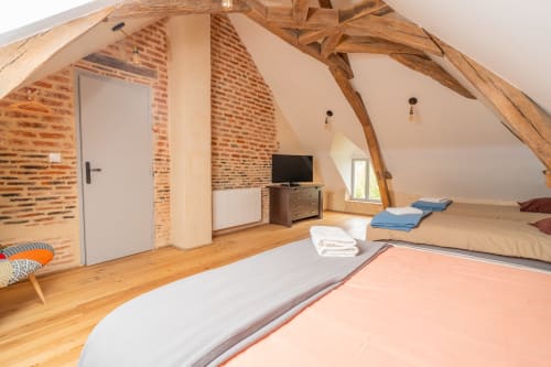 Chambre du cottage Le Charme avec poutres apparentes, murs de brique et plusieurs lits à Vacances en Touraine