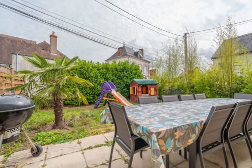 Terrasse du cottage Le Charme à Souvigny-de-Touraine avec table de jardin, grill, toboggan et verdure luxuriante