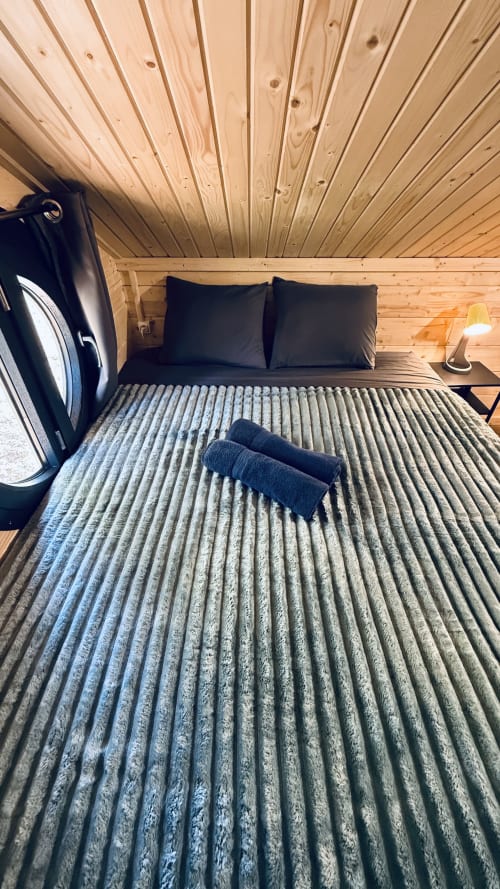 Accogliente camera da letto in lodge in legno con biancheria grigia rigata, cuscini neri e soffitto in pino rustico a Cabanes du Belvédère