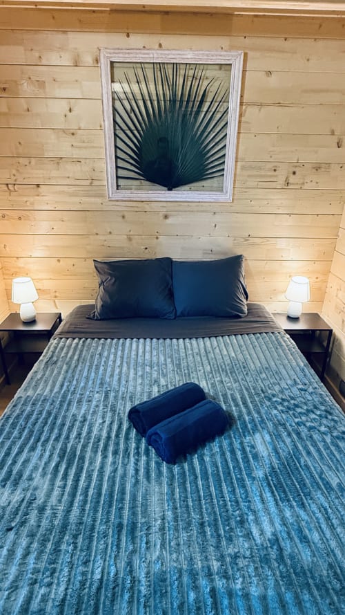 Camera moderna presso Lodge l'EPERVIER con pareti in legno, letto matrimoniale con cuscini blu, comodini scuri e lampade bianche