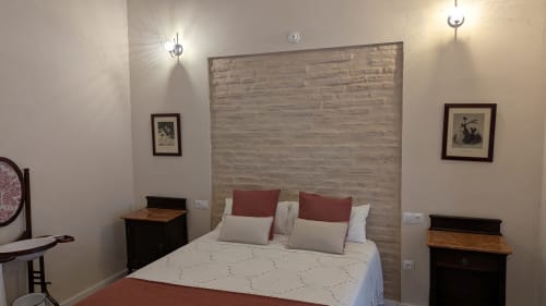 Dormitorio moderno en Villas Vacacionales Sevilla con pared de piedra, almohadas rojas y luminarias contemporáneas