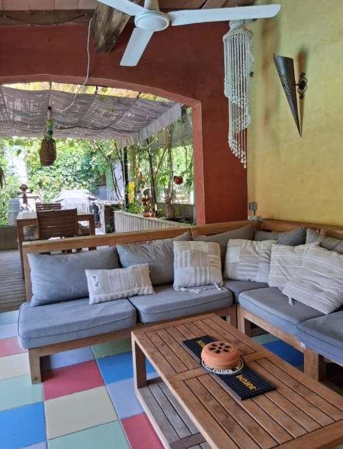 Cozy sitting area at La Conciergerie De Franck villa with wooden furniture, blue cushions, colorful rug, and garden view