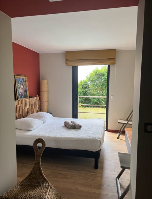 Modern villa bedroom at La Conciergerie De Franck with pool view, red accent wall, glass doors opening to garden, white