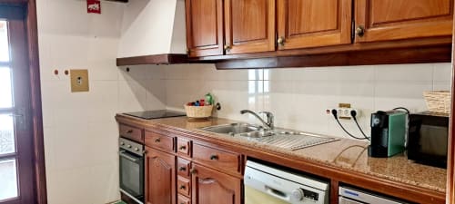 Cozinha em madeira com bancadas de granito, pia, fogão e eletrodomésticos na Casa Da Avó Ilda em Matosinhos