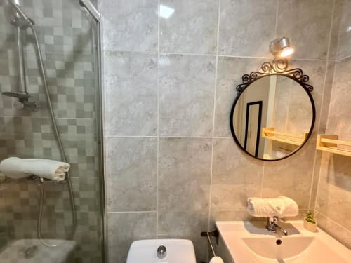 Baño moderno del apartamento Holibai Xacobe en Baiona con ducha alicatada, lavabo, espejo decorativo y toallero