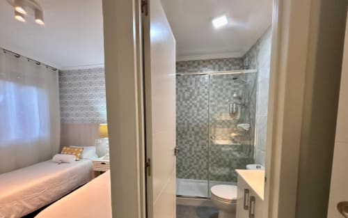 Dormitorio de apartamento moderno con baño ensuite y ducha de cristal en Baiona