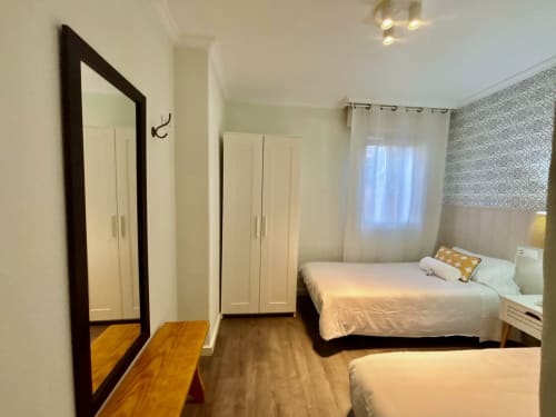 Dormitorio moderno en Holibai, Baiona, con dos camas, armario, espejo y ventana con vista a la ciudad