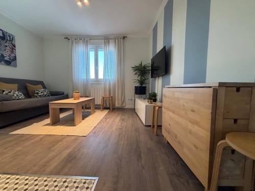Moderno salón de apartamento en Sabaris, Baiona con muebles de madera, sofá, televisor y zona de cocina