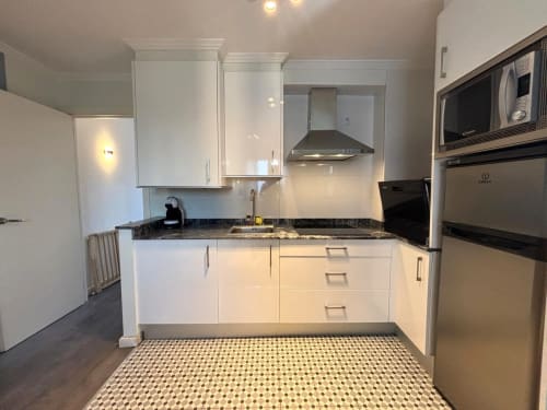 Moderna cocina blanca con encimeras oscuras, electrodomésticos de acero inoxidable y suelo de azulejos estampados en el apartamento Holibai, Baiona