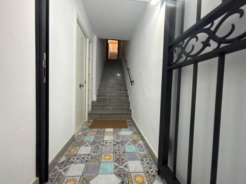 Entrada del pasillo del apartamento Holibai en Baiona con baldosas decorativas, paredes blancas, escalera y ornamentación negra