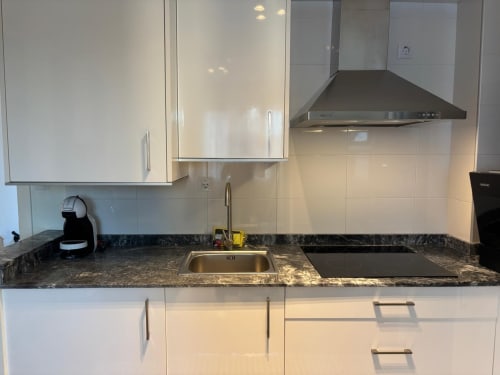 Moderna cocina del apartamento Holibai en Baiona con gabinetes blancos, encimera de granito, fregadero, vitrocerámica y rango de acero inoxidable