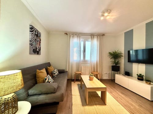 Salón moderno y luminoso del apartamento Holibai Xacobe en Baiona con sofá gris, mesa de madera, TV y vistas al balcón