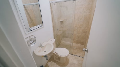 Baño moderno con ducha de azulejos beige, lavabo blanco, inodoro y espejo en el hotel Olamar Living de Coveñas, Colombia