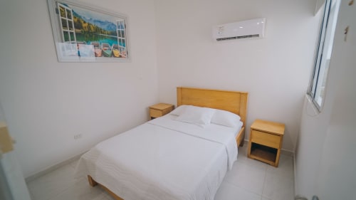 Dormitorio luminoso en hotel Olamar Living de Coveñas con cama de madera, ropa blanca, mesillas y aire acondicionado