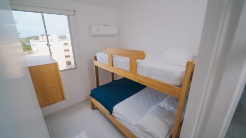 Dormitorio luminoso con literas de madera, ropa de cama blanca, manta azul oscuro y vistas al balcón en el hotel Olamar Living