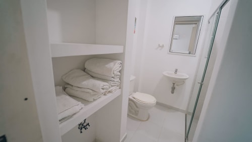 Baño limpio con inodoro, lavamanos, espejo y estantes con toallas dobladas en el hotel Olamar Living de Santiago de Tolú