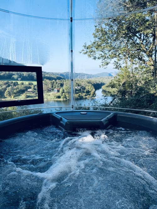 Vasca idromassaggio con acqua frizzante che affaccia sul fiume Ain e sulla valle boschiva presso Cabanes et lodges du Belvédère