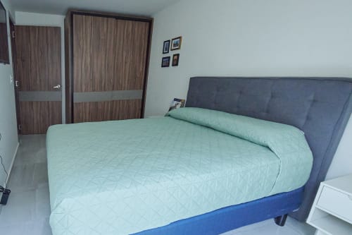 Moderno dormitorio en apartamento Pares Homes Ciudad de México con cama queen, cabecera gris, ropa de cama clara y puertas de armario de madera.