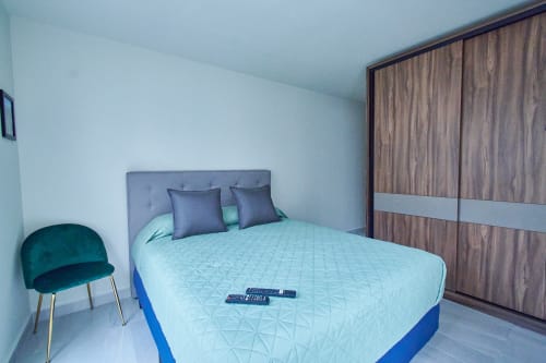 Recámara moderna en apartamento de Pares Homes Ciudad de México con cama matrimonial, silla de acentos en turquesa y armario de madera