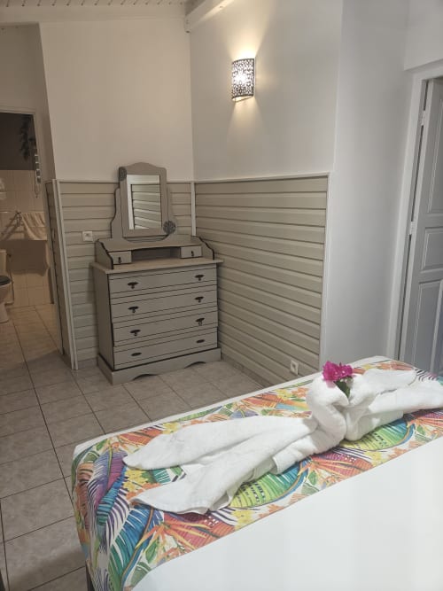 Bedroom at Gites Kaladja with colorful bedspread, rolled white towels, wooden dresser, and wall sconces in Port-Louis