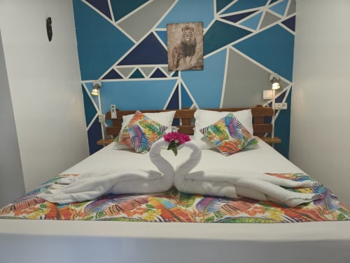 Romantic bedroom at Gites Kaladja with geometric blue headboard, white swan towel art, colorful pillows, and tropical bedding